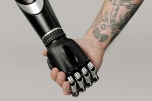 Tattooed human hand holding a prosthetic hand in a studio setting, symbolizing connection and technology.